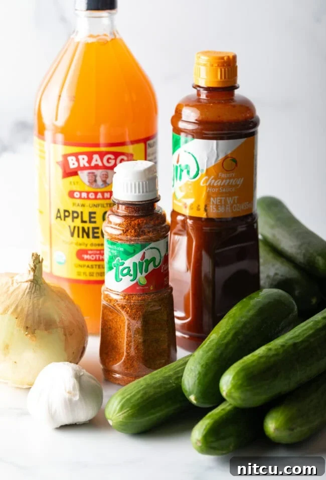 Chamoy Drenched Pickles 5 Recipe ingredients: Jars of apple cider vinegar, Tajin seasoning, and chamoy sauce. Also several small cucumbers, a whole onion, and head of garlic.