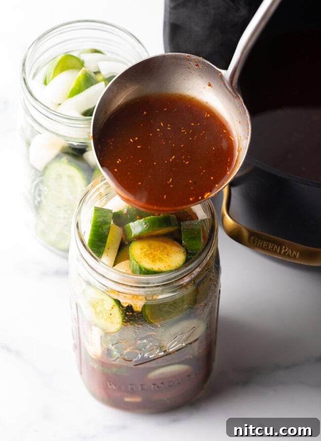 Chamoy Drenched Pickles 8 Pouring red liquid from a metal ladle into a glass jar filled with pickle slices.