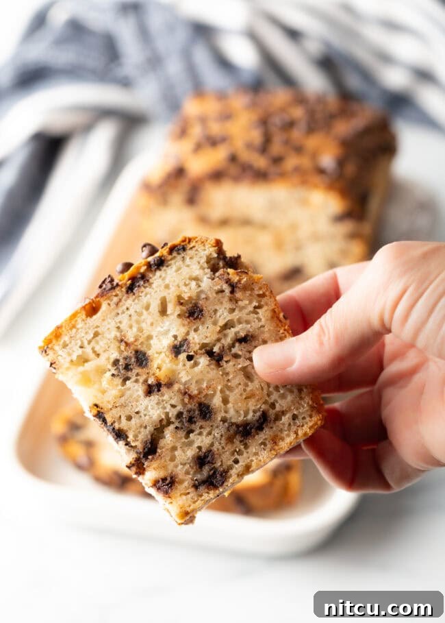 Hand holding a slice of chocolate chip ice cream bread.