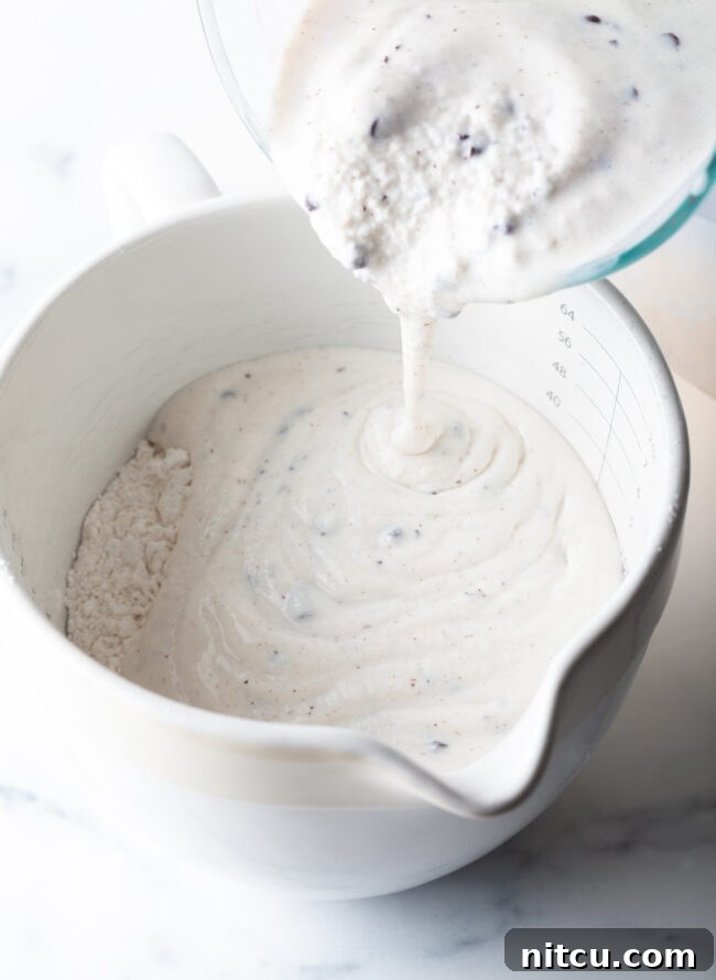 Adding melted ice cream to a white mixing bowl with flour.