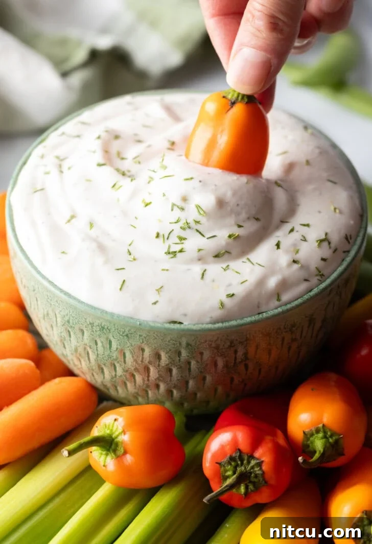 Mini orange pepper dipping into a small green bowl of white cottage cheese dip.