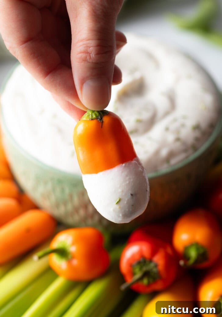 Mini orange pepper dipped into a small green bowl of white cottage cheese dip. Hand is holding dip-covered pepper to camera.