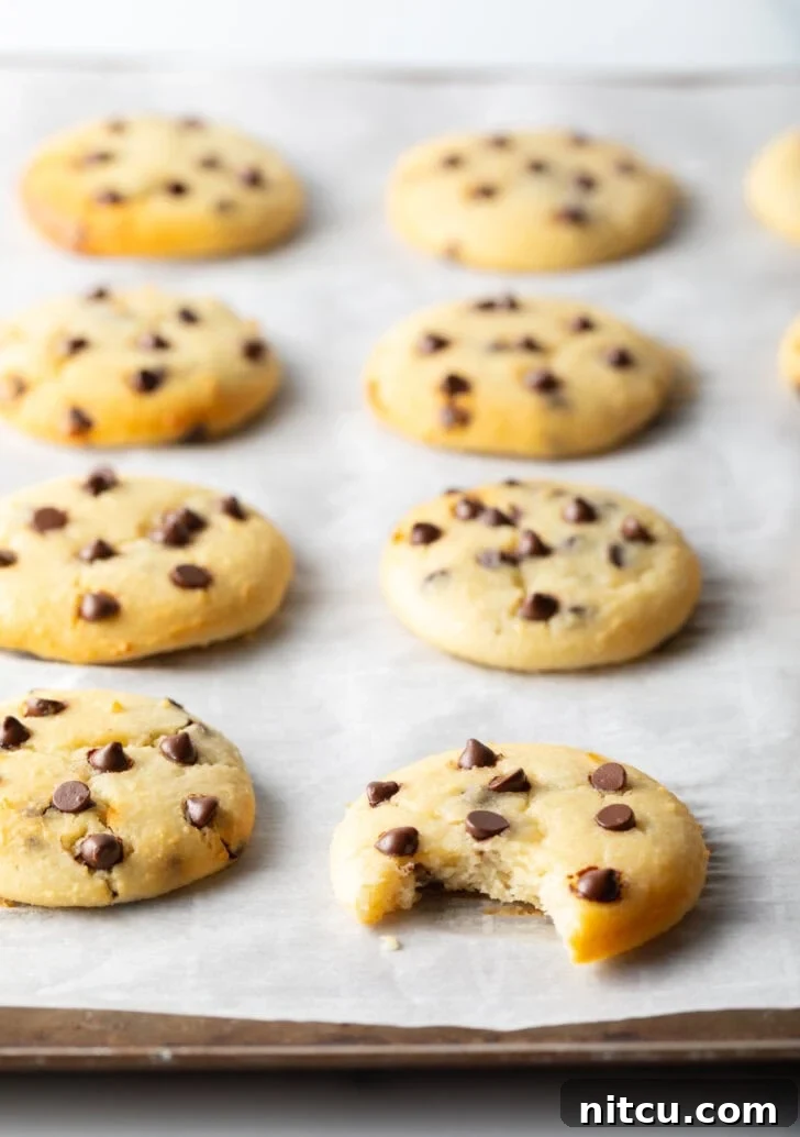 Wholesome Cookie Dough Delight 4 8 cottage cheese chocolate chip cookies cooling on a baking sheet. A front cookie has a bite missing.