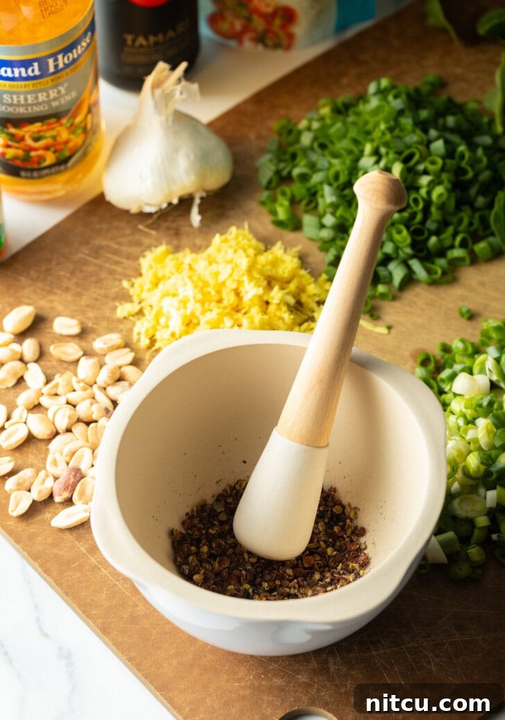 Recipe ingredients: Peppercorns with a mortal and pestel, cutting board with piles of sliced garlic, minced ginger, sliced onions, and spinach.