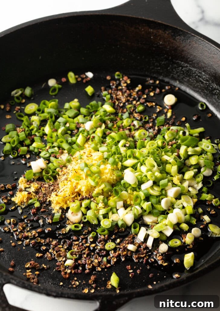 Spicy Szechuan peppercorns, ginger, and green sliced onions in a cast iron skillet.