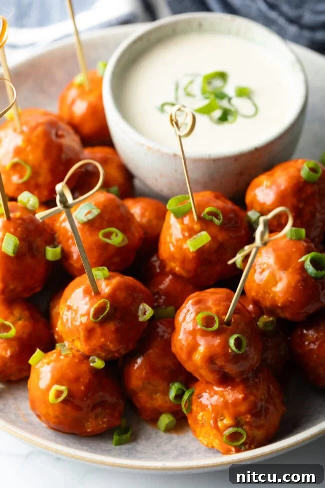 Plate of buffalo chicken meatballs skewered with serving toothpicks, nestled next to a white dish of ranch dressing dipping sauce.