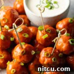 Plate of buffalo chicken meatballs skewered with serving toothpicks, nestled next to a white dish of ranch dressing dipping sauce.