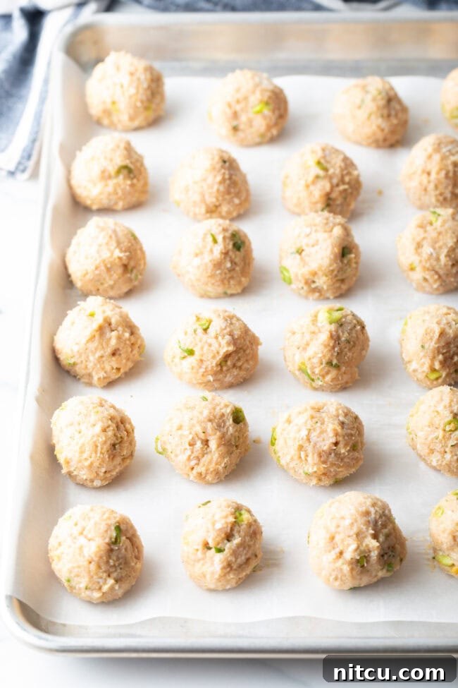16 raw meat balls on a baking sheet lined with parchment paper.