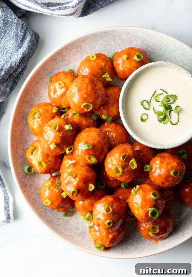 Plate of buffalo chicken meatballs nestled next to a white dish of ranch dressing dipping sauce.