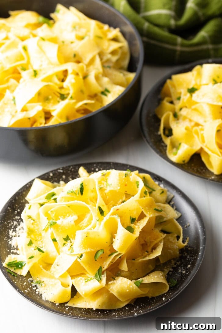 Irresistible Garlic Butter Noodles 11 Top down view of a black bowl loaded with wide pappardelle pasta topped with fresh herbs and grated parmesan cheese.