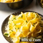 Irresistible Garlic Butter Noodles 13 Top down view of a black bowl loaded with wide pappardelle pasta topped with fresh herbs and grated parmesan cheese.