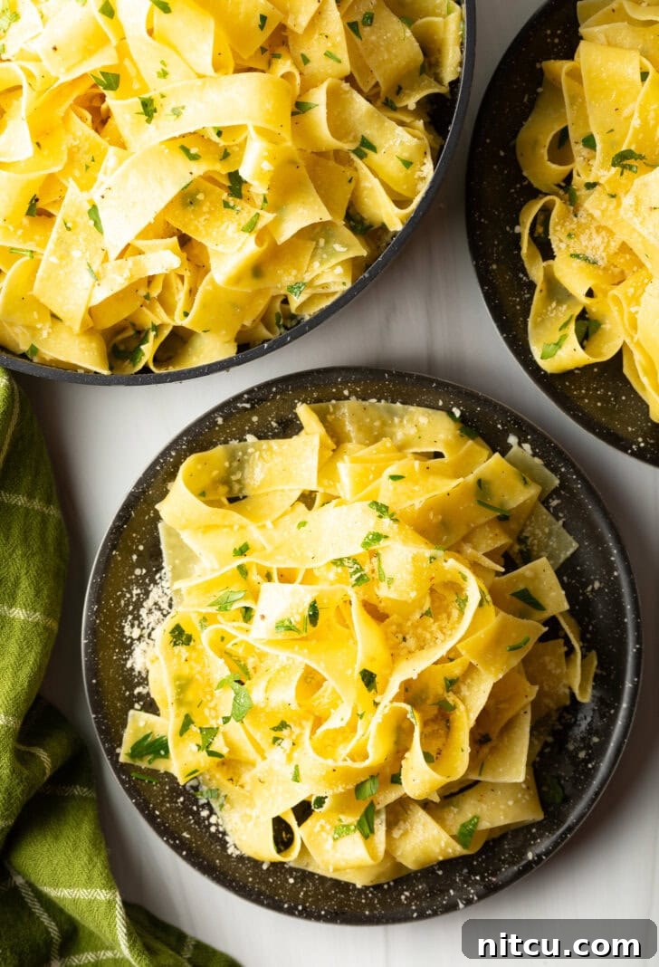 Irresistible Garlic Butter Noodles 3 Top down view of a black bowl loaded with wide pappardelle pasta topped with fresh herbs and grated parmesan cheese.