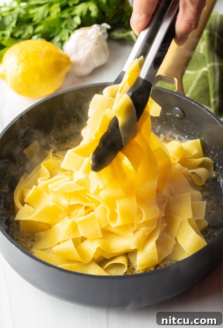 Irresistible Garlic Butter Noodles 6 Tongs tossing pappardelle pasta with butter and garlic.