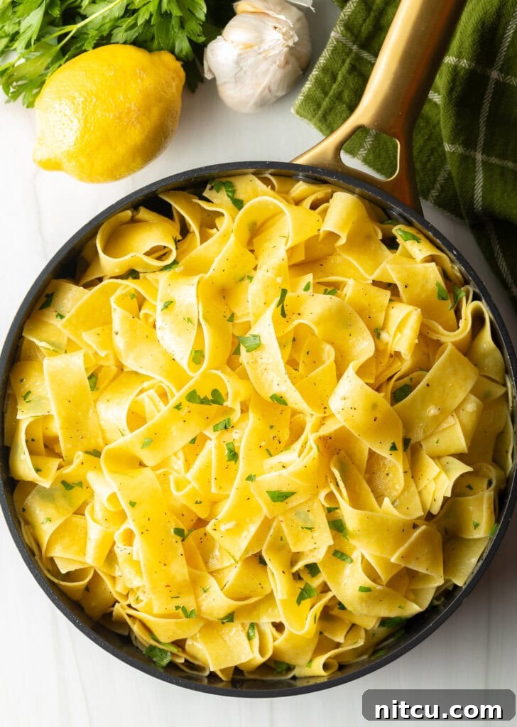 Irresistible Garlic Butter Noodles 9 Top down view of a black bowl loaded with wide pappardelle pasta topped with fresh herbs and grated parmesan cheese.