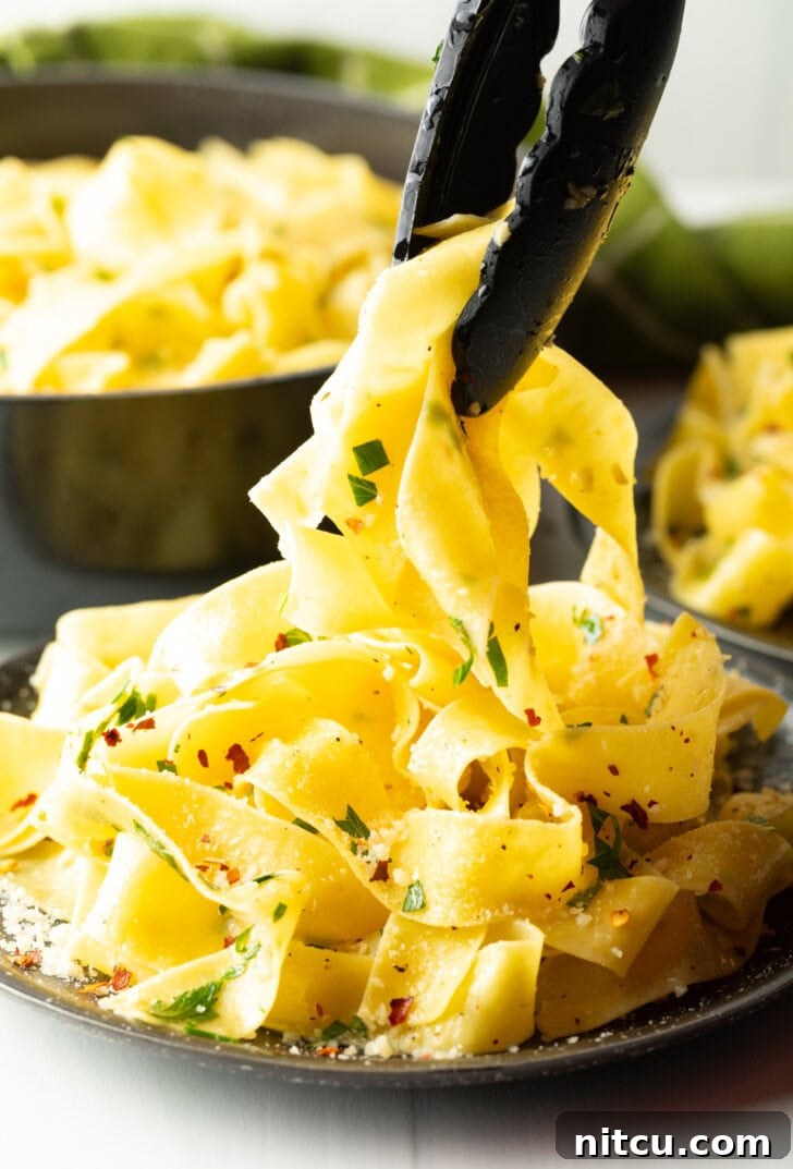 Irresistible Garlic Butter Noodles 10 Tongs grabbing several wide noodles from a black bowl