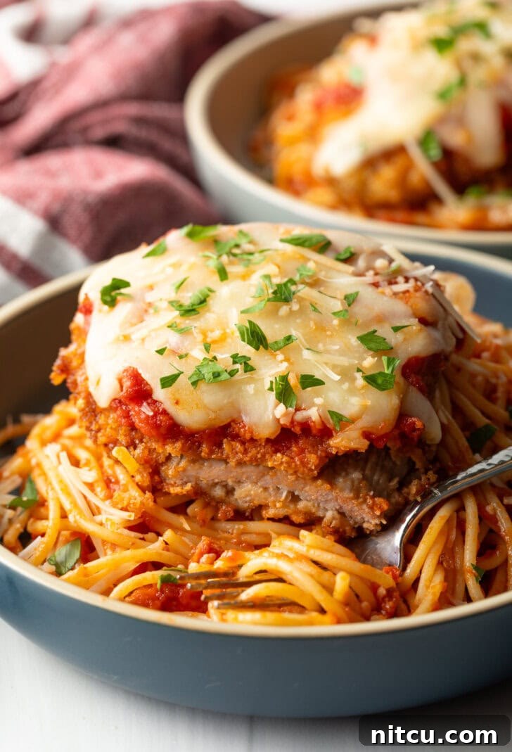 A cutlet of veal parmesan on top of spaghetti. A bite has been removed from the veal to show the juicy inside.