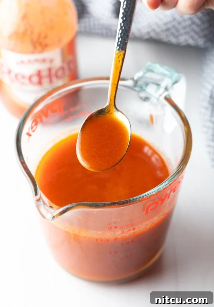 The Best Homemade Buffalo Wing Sauce 2 Spoon drizzling buffalo sauce from a large glass measuring cup.