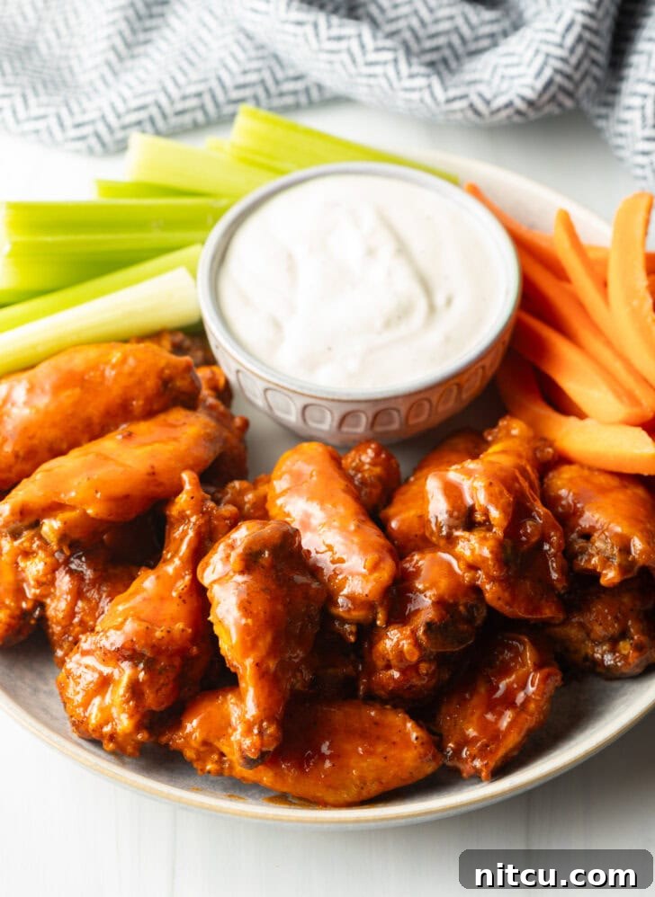 The Best Homemade Buffalo Wing Sauce 11 Plate of saucy buffalo chicken wings. On the plate is also a ramekin of ranch dressing, a pile of carrot sticks, and a pile of celery sticks.