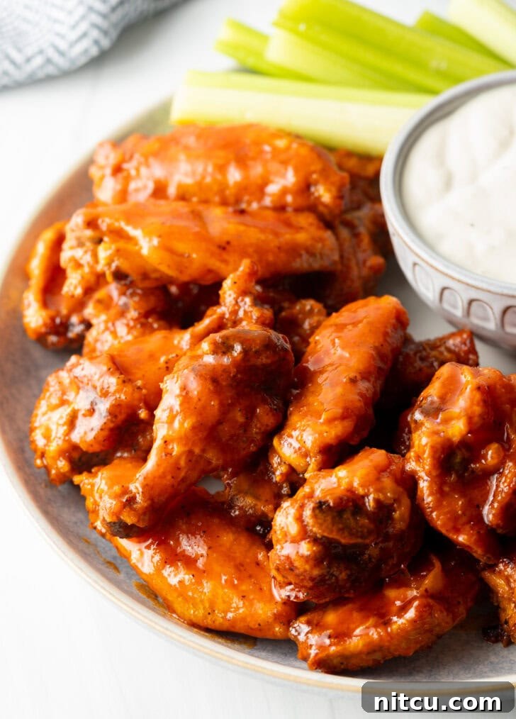 The Best Homemade Buffalo Wing Sauce 3 Plate of saucy buffalo chicken wings. On the plate is also a ramekin of ranch dressing, a pile of carrot sticks, and a pile of celery sticks.