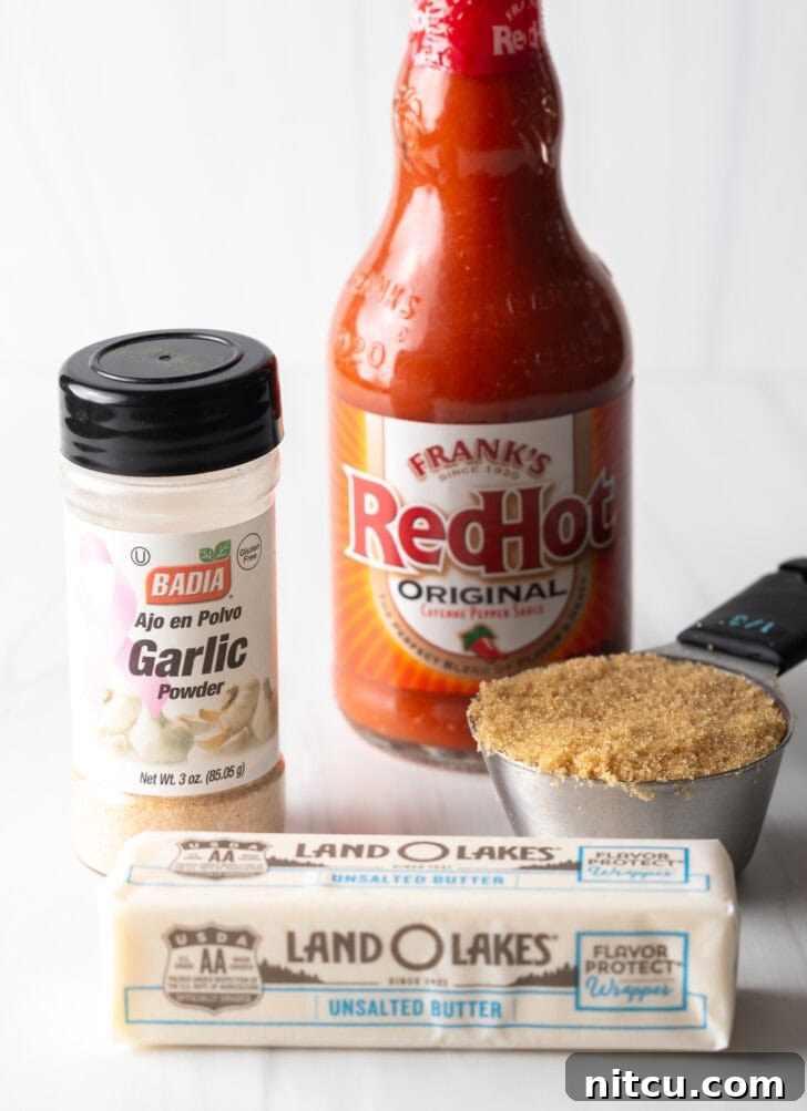 The Best Homemade Buffalo Wing Sauce 4 Recipe ingredients on a white backdrop: Bottle of Frank's RedHot, metal scoop of brown sugar, container of garlic seasoning, and a stick of butter.