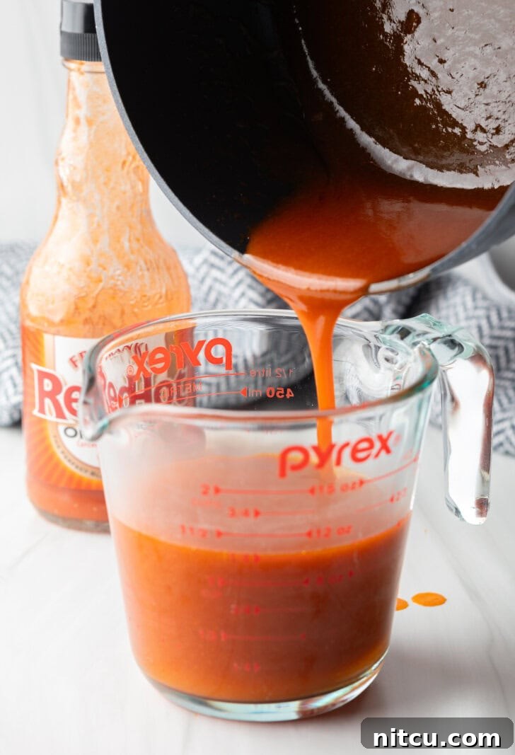 The Best Homemade Buffalo Wing Sauce 7 Pouring homemade buffalo sauce from a black sauce pot into a large glass measuring cup.