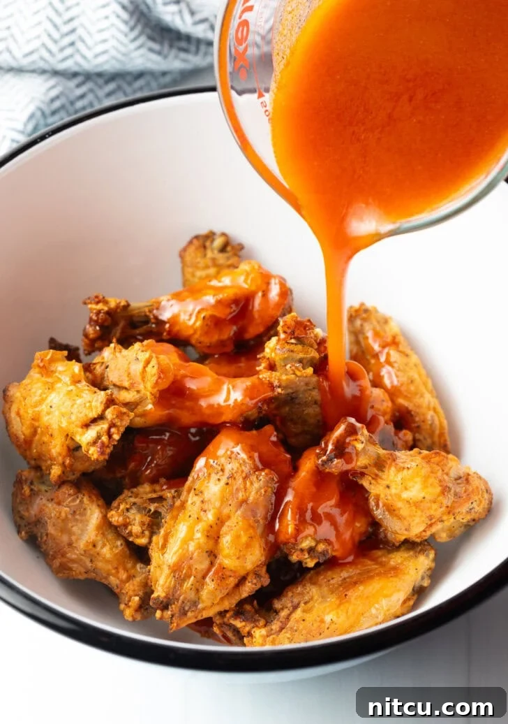 The Best Homemade Buffalo Wing Sauce 8 Pouring spicy buffalo sauce from a measuring cup onto fried chicken wings in a bowl.