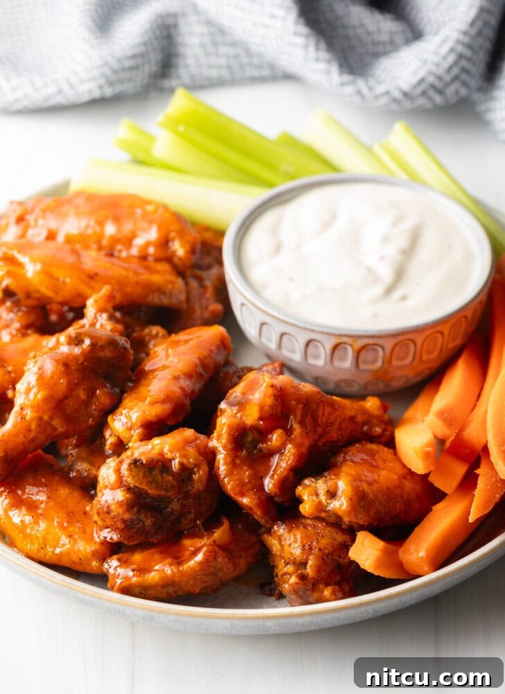 The Best Homemade Buffalo Wing Sauce 9 Plate of saucy buffalo chicken wings. On the plate is also a ramekin of ranch dressing, a pile of carrot sticks, and a pile of celery sticks.