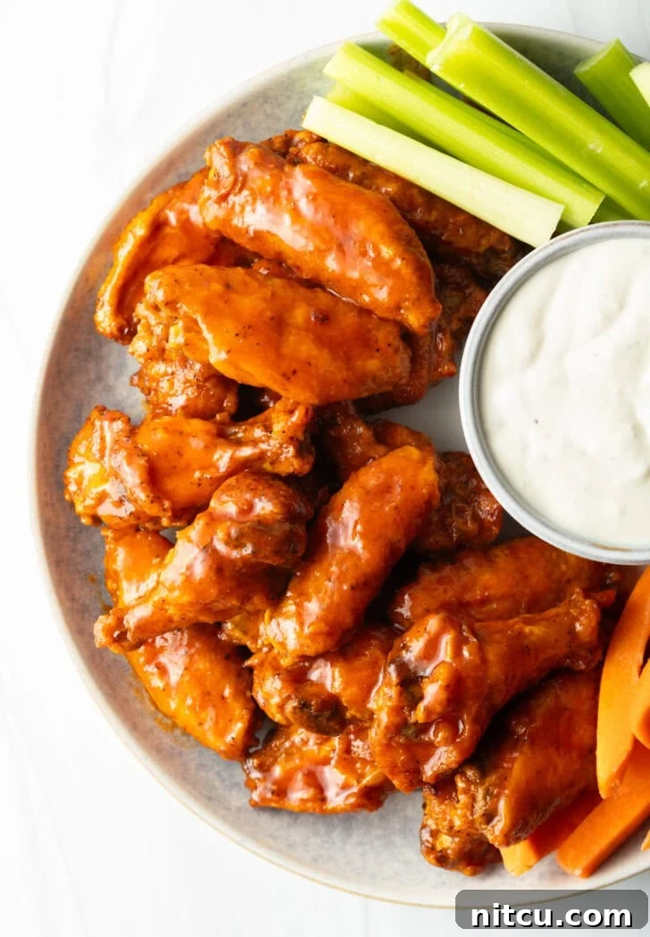 The Best Homemade Buffalo Wing Sauce 10 Plate of saucy buffalo chicken wings. On the plate is also a ramekin of ranch dressing, a pile of carrot sticks, and a pile of celery sticks.