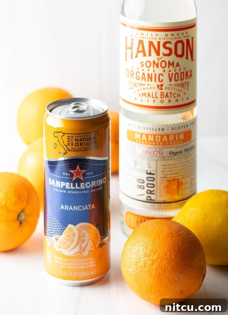 Can of orange soda, bottle of vodka, several fresh oranges and lemons all around.