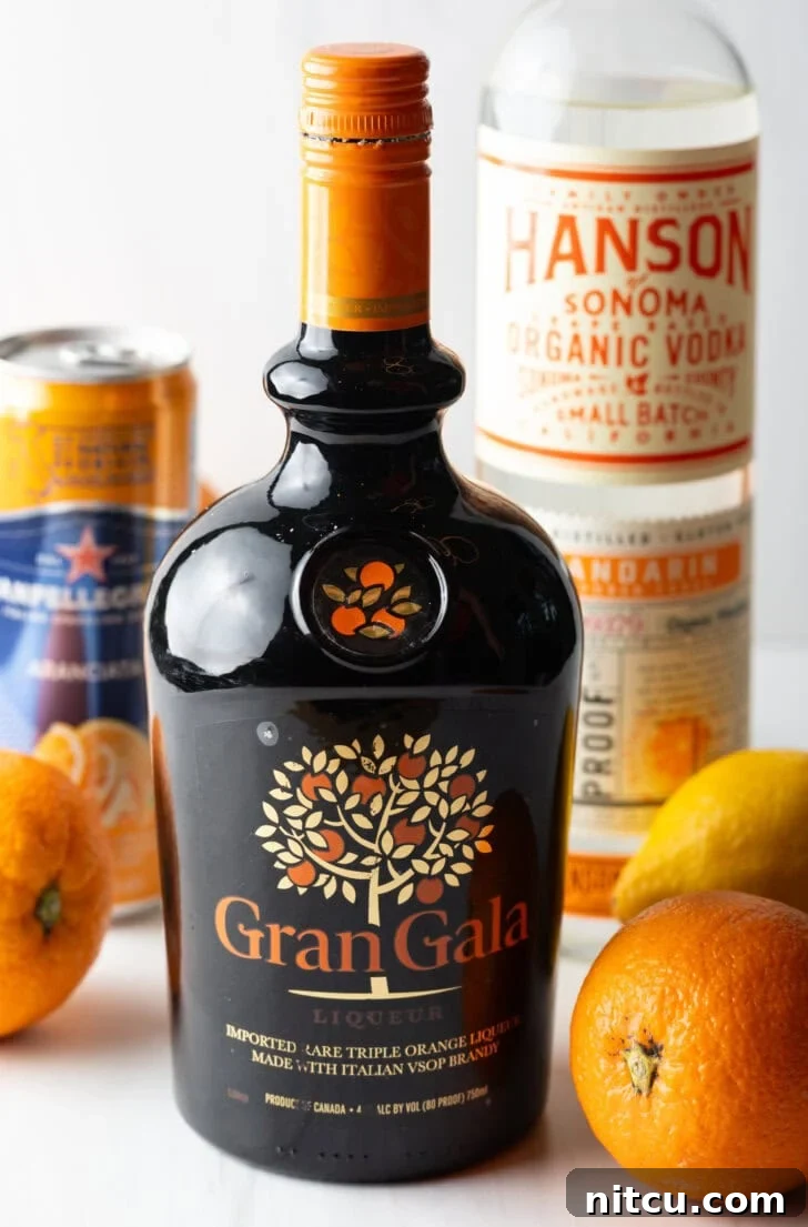 Recipe ingredients: Bottle of Grangala in the front, fresh oranges, bottle of vodka, and can of orange soda in the background.
