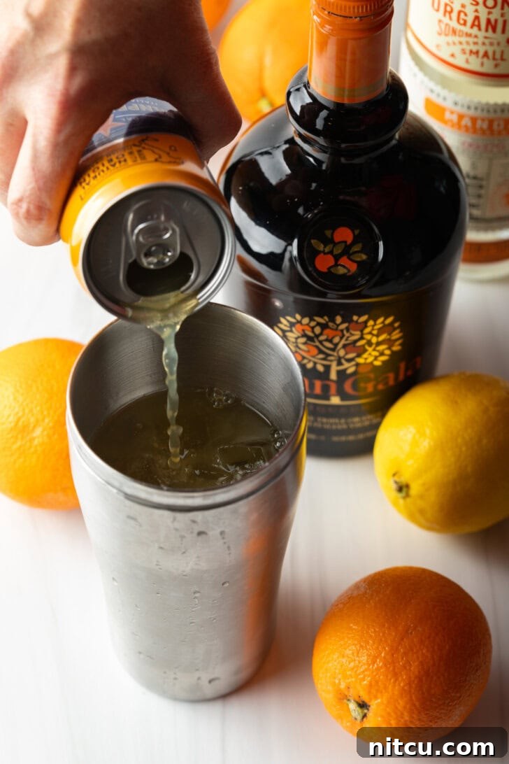 Hand pouring orange soda into metal cocktail shaker.