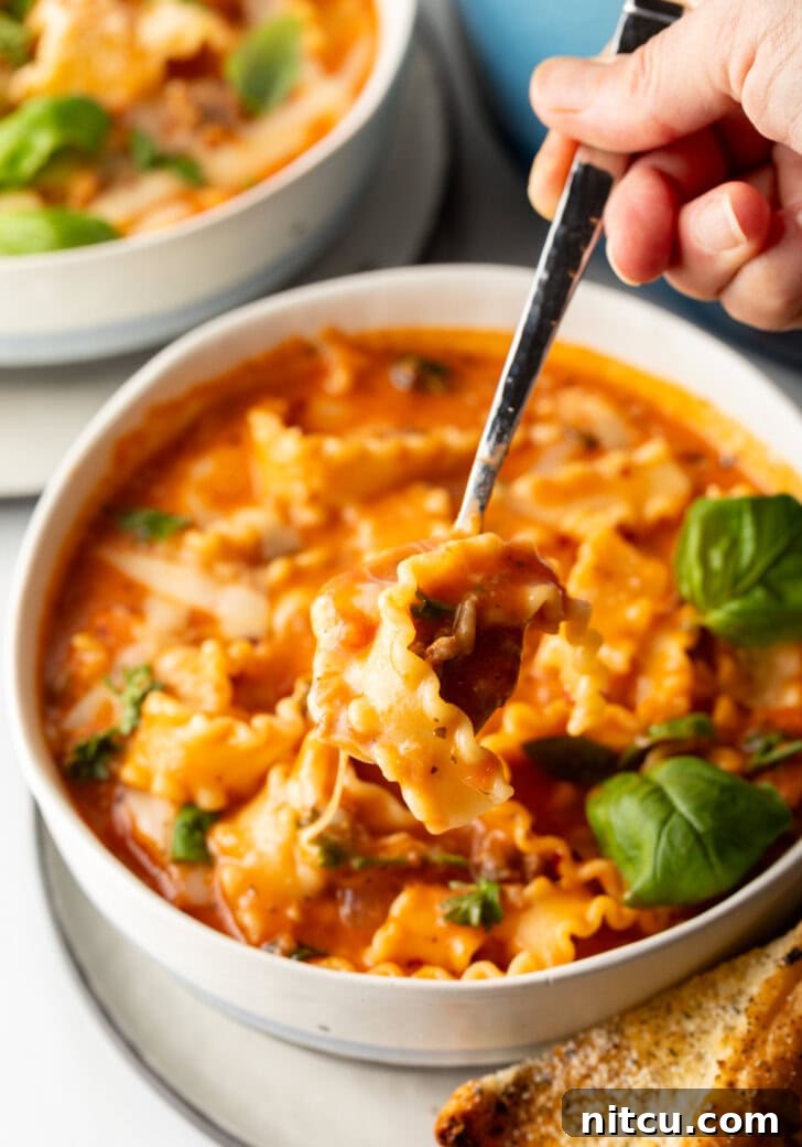 One-Pot Lasagna Delight 12 A spoon lifts a delicious bite of cheesy tomato soup with pasta and sausage, showcasing the delightful blend of textures and flavors.