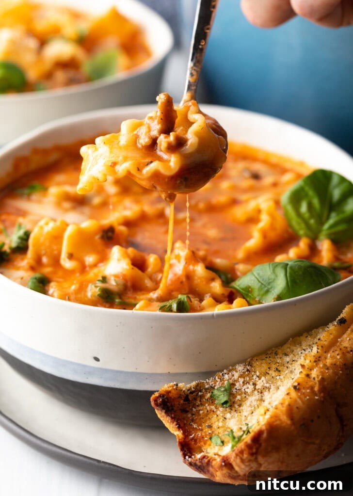 One-Pot Lasagna Delight 4 A spoon gracefully scoops a hearty bite of tomato and cheesy lasagna soup, showcasing the perfectly cooked pasta, savory sausage, and rich broth.