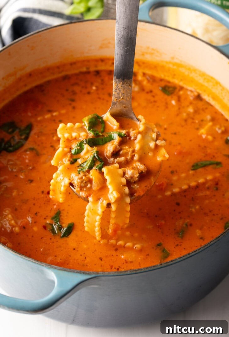 One-Pot Lasagna Delight 9 A ladle filled with savory lasagna soup, held above the pot, showcasing its inviting texture and readiness to be served.
