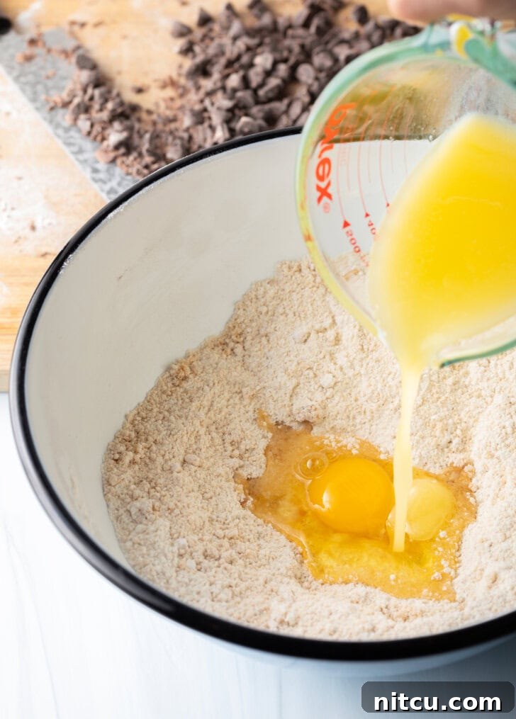 Ultimate Chocolate Chip Cookie Cake 5 Adding melted butter to the white mixing bowl with dry ingredients