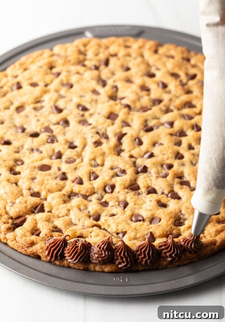 Ultimate Chocolate Chip Cookie Cake 10 Piping chocolate frosting along the edge of the cookie cake.