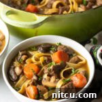 Ultimate Beef Noodle Soup 13 White bowl of noodle soup with meat and veggies.