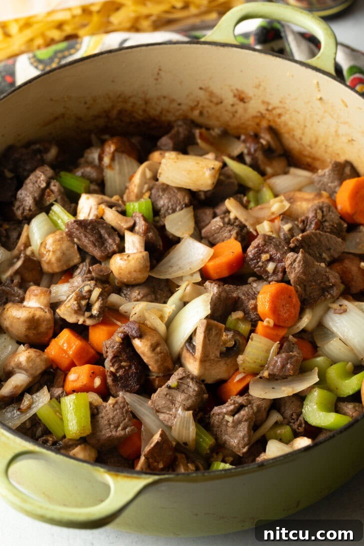 Ultimate Beef Noodle Soup 5 Searing beef chunks and veggies in a large cooking pot.