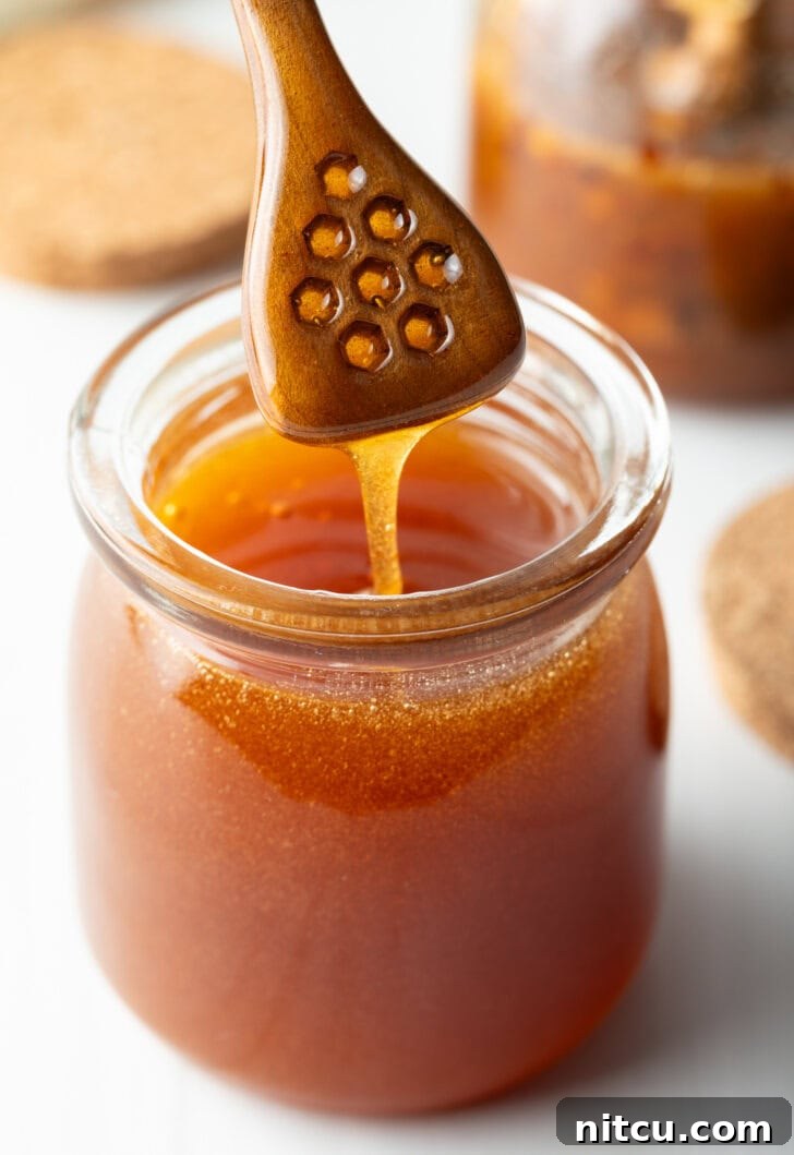 Jar of homemade hot honey with a wooden honey dipper showing a scoop of honey to camera.
