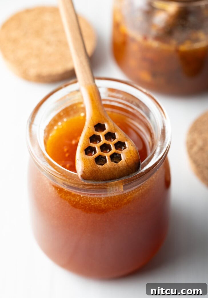 Jar of homemade hot honey with a wooden honey dipper showing a scoop of honey to camera.