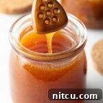 Jar of homemade hot honey with a wooden honey dipper showing a scoop of honey to camera.