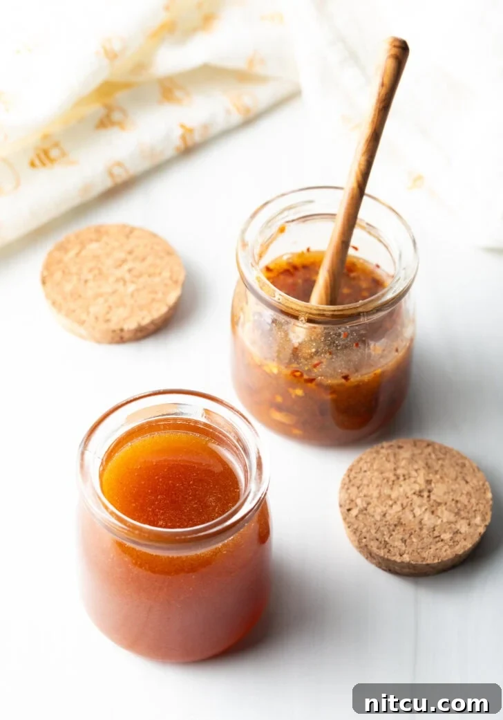 Two open small glass jars of hot honey. A wood honey spoon is in the far jar to the right.