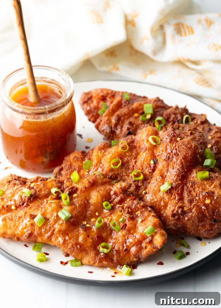 Plate of chicken tenders with small glass jar of hot honey to the side, with a wooden honey spoon in the jar.