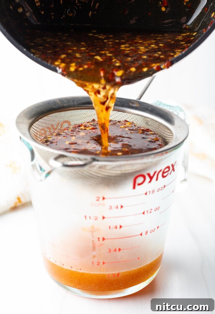 Pouring mixture from the black sauce pot into a metal sieve over a glass measuring cup.