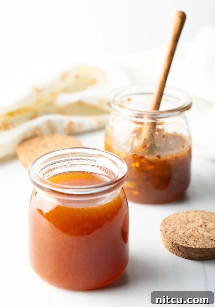 Two open small glass jars of hot honey. A wood honey spoon is in the far jar to the right.