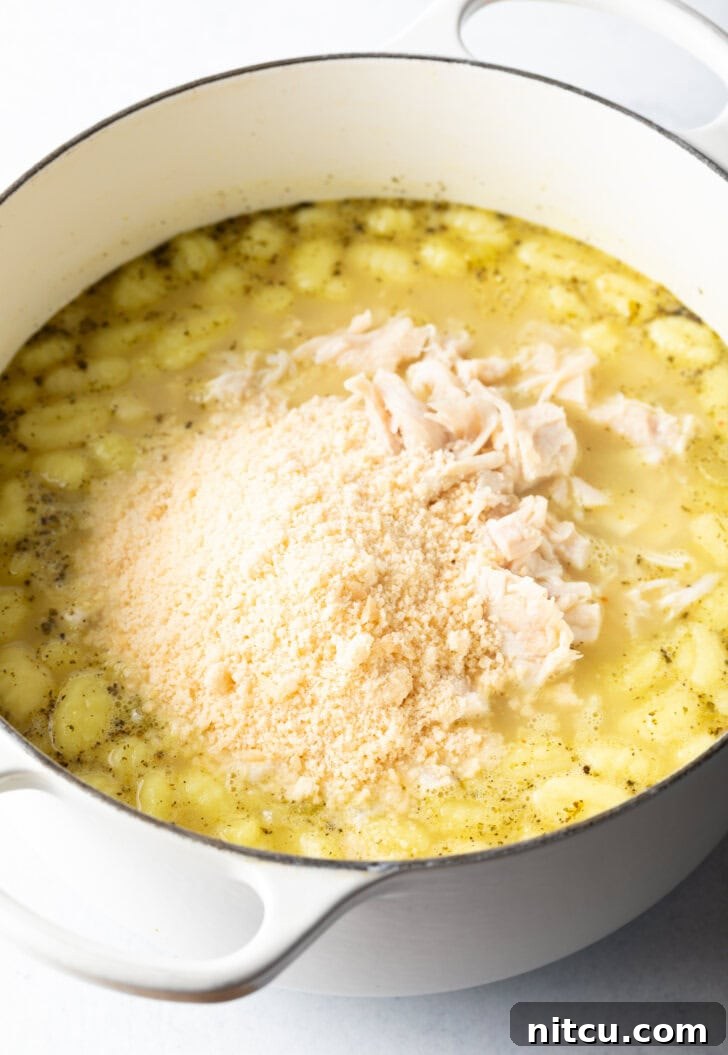 A hand generously adding grated Parmesan cheese into the creamy soup pot, enhancing its richness.