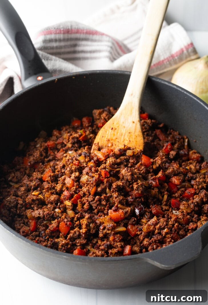 Smothered Chili Cheese Fries 5 A wooden spoon stirring a vibrant, simmering chili in a deep, black cast iron skillet. The chili is rich with meat, vegetables, and spices, indicating it's in the process of developing deep flavors.