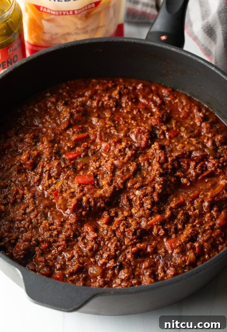 Smothered Chili Cheese Fries 6 A close-up shot of a deep, black cast iron skillet filled with freshly made, rich, and hearty homemade chili. The chili has a thick consistency, with visible chunks of meat and vegetables, ready to be served.