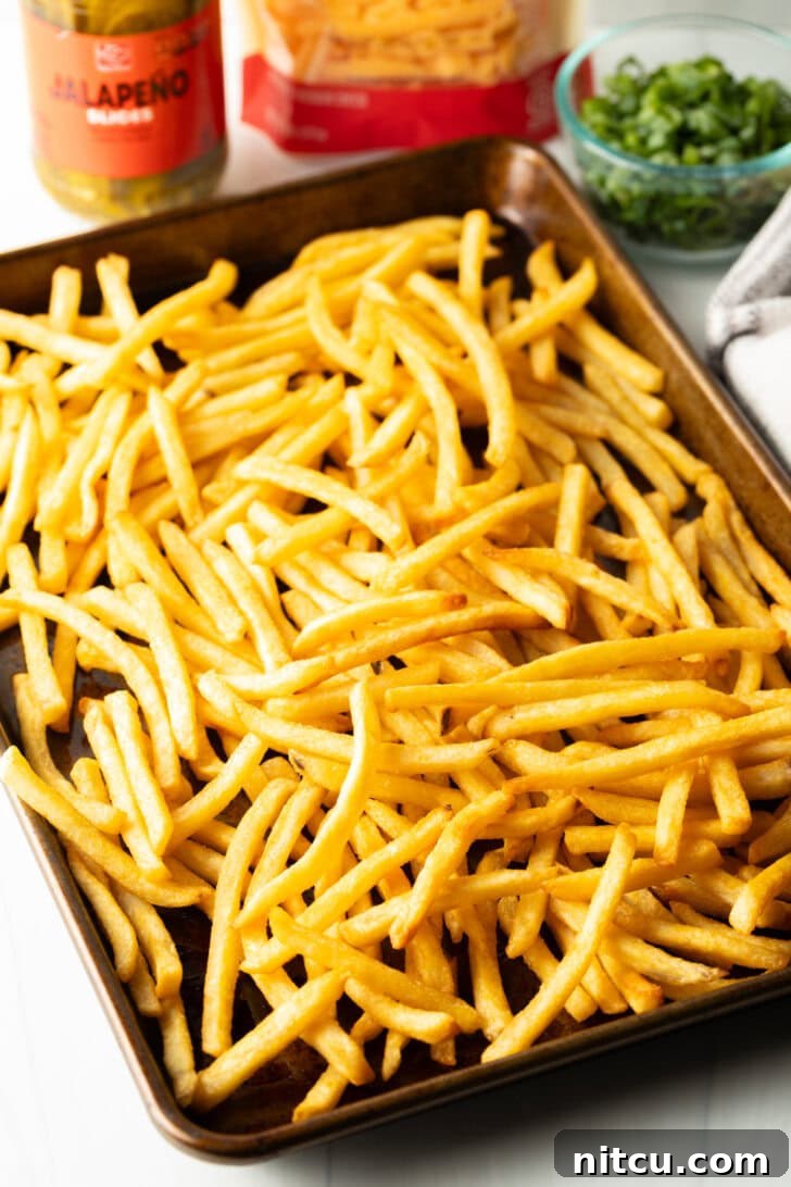 Smothered Chili Cheese Fries 7 A large baking sheet generously loaded with golden, crispy french fries, fresh out of the oven or fryer. They appear perfectly cooked and seasoned, ready for assembly.