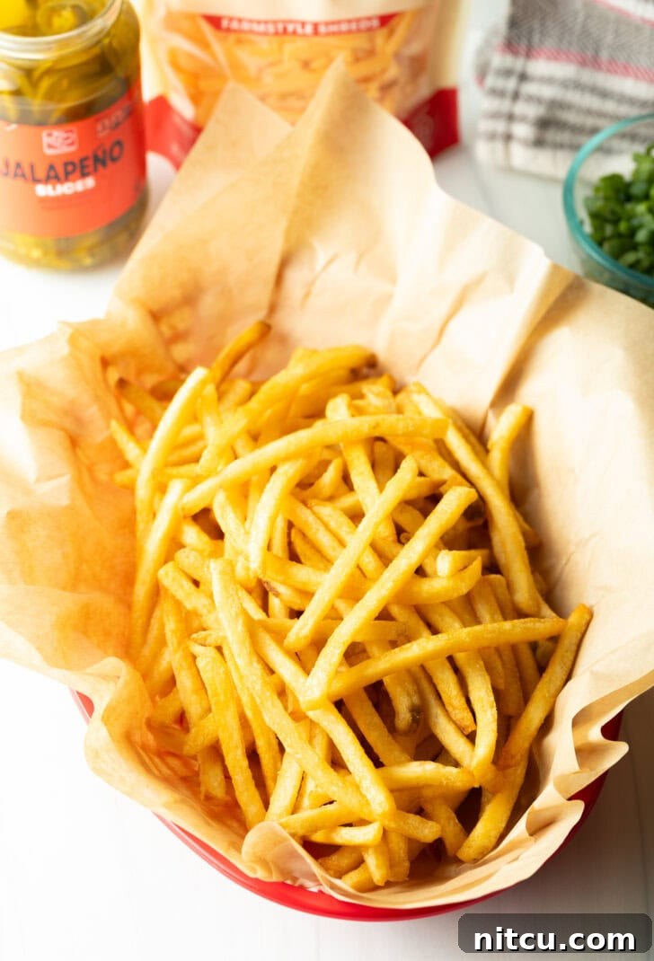 Smothered Chili Cheese Fries 8 A rustic basket lined with parchment paper, filled with a generous portion of freshly cooked, golden, and crispy french fries, ready for the delicious toppings.